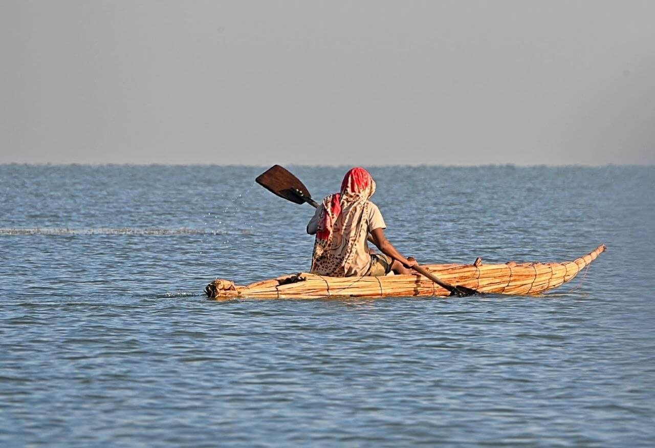 Person paddling a traditional papyrus reed boat across calm waters of Lake Tana in Ethiopia